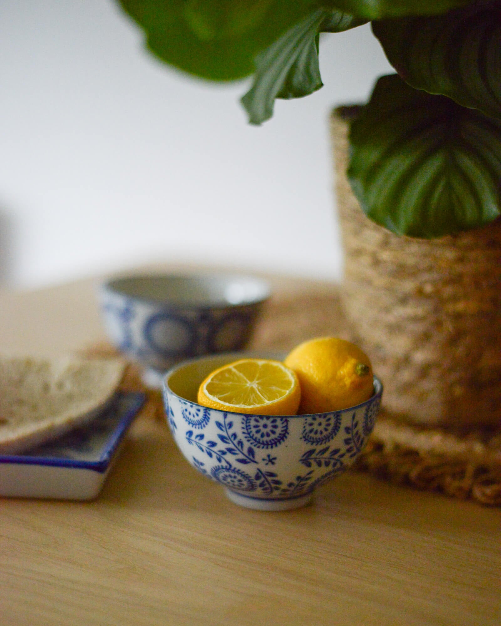 Blue and white patterned decorative ceramic bowls with lemons on a wooden surface, plant in the background