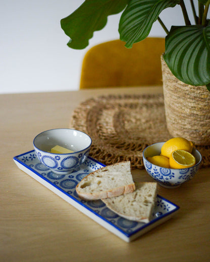 Bread slices on a decorative rectangular plate with small ceramic bowls of lemons and a woven basket on a wooden table.