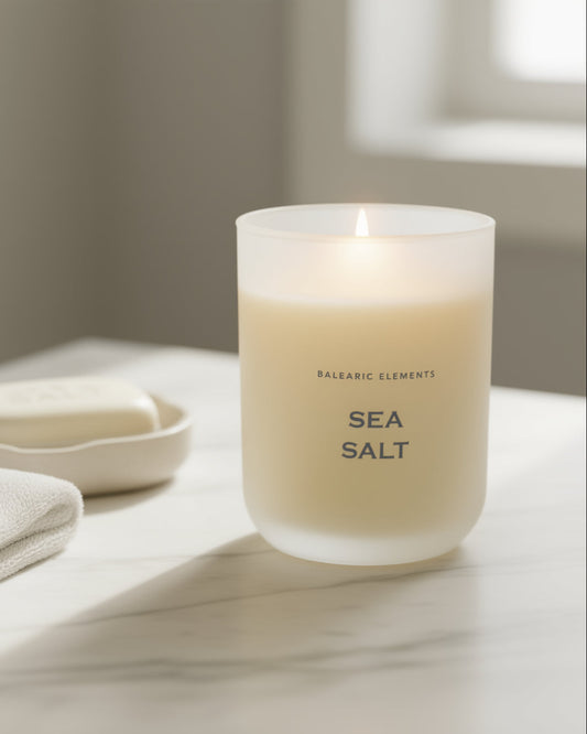 Scented candle labeled 'Sea Salt' on a marble surface with a towel and soap dish in the background.