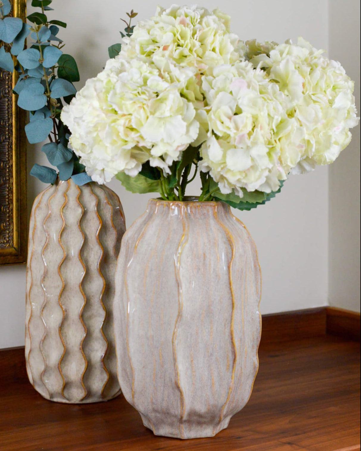Two decorative vases with textured surfaces holding white flowers on a wooden table.