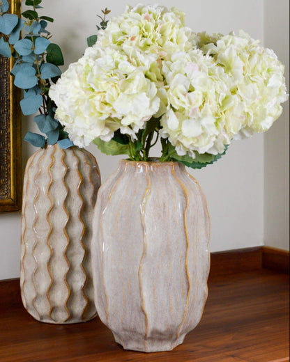 Two decorative vases with textured surfaces holding white flowers on a wooden table.
