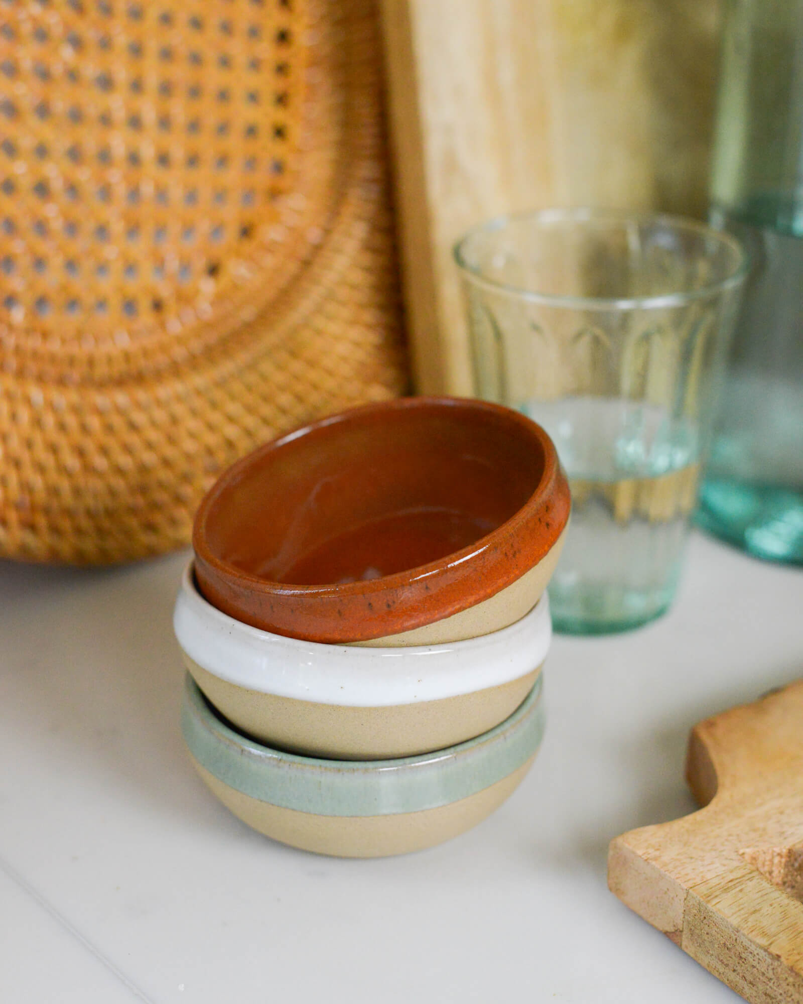 Stack of ceramic stoneware dipping bowls with a woven rattan plate and glass in the background