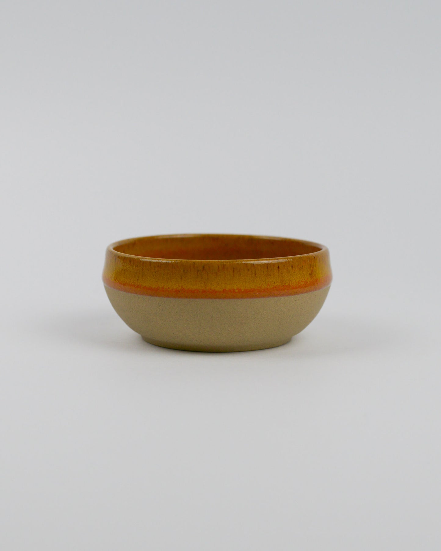 Small ceramic stoneware dipping bowl with a yellow rim on a white background