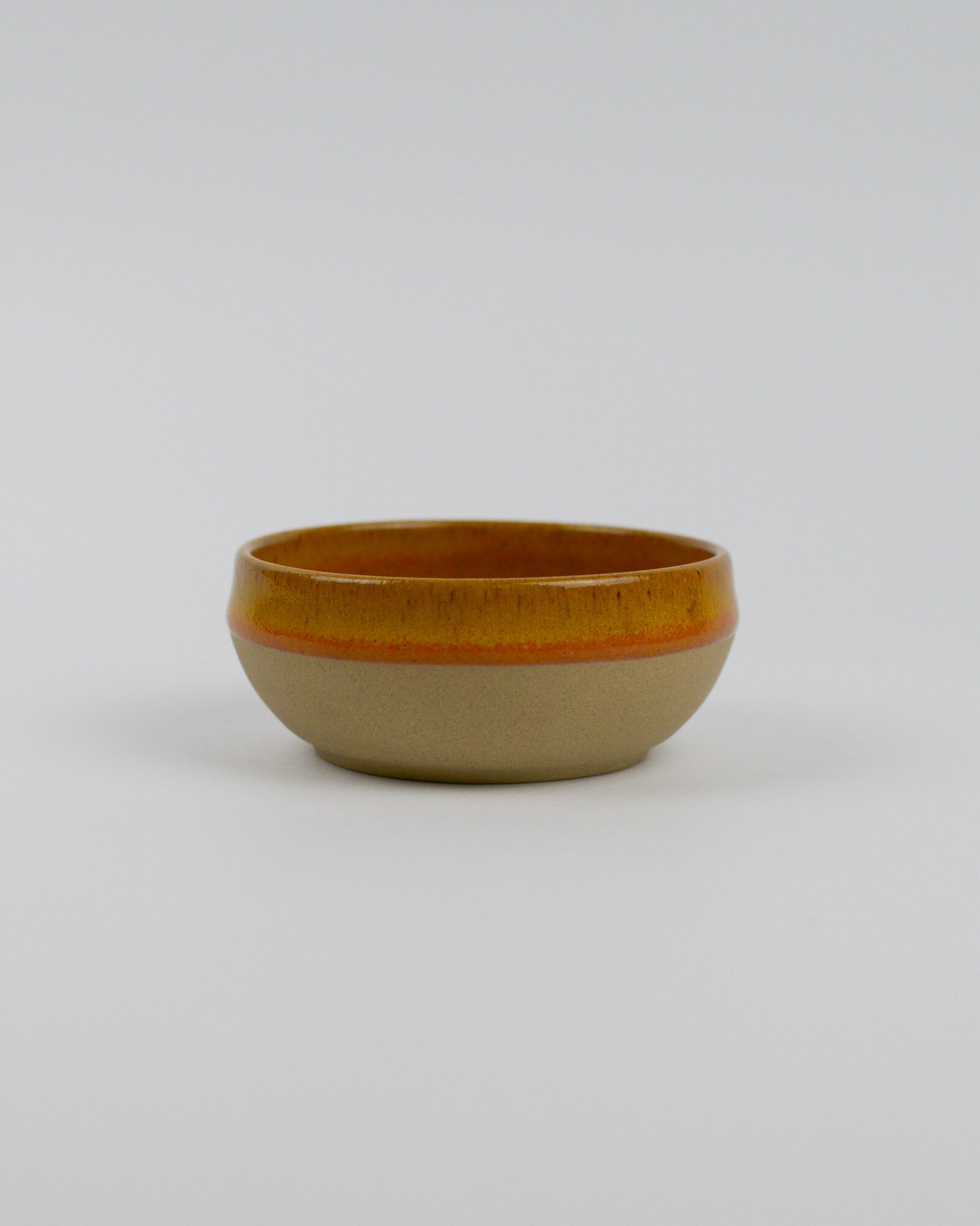 Small ceramic stoneware dipping bowl with a yellow rim on a white background
