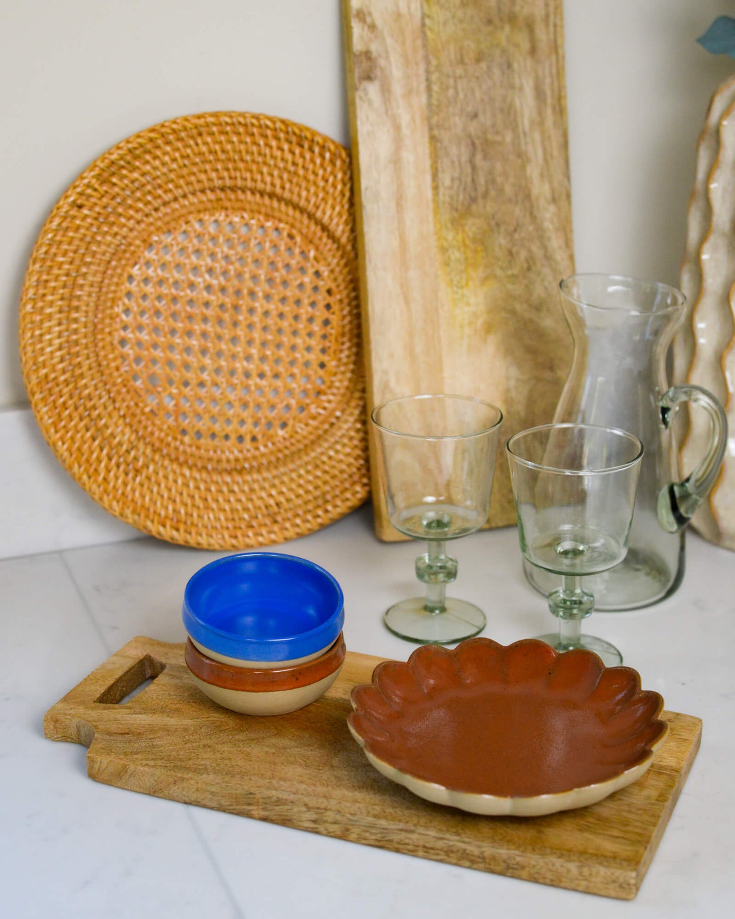 Dishes including a blue stoneware dipping bowl, brown plate, and glassware on a wooden tray.