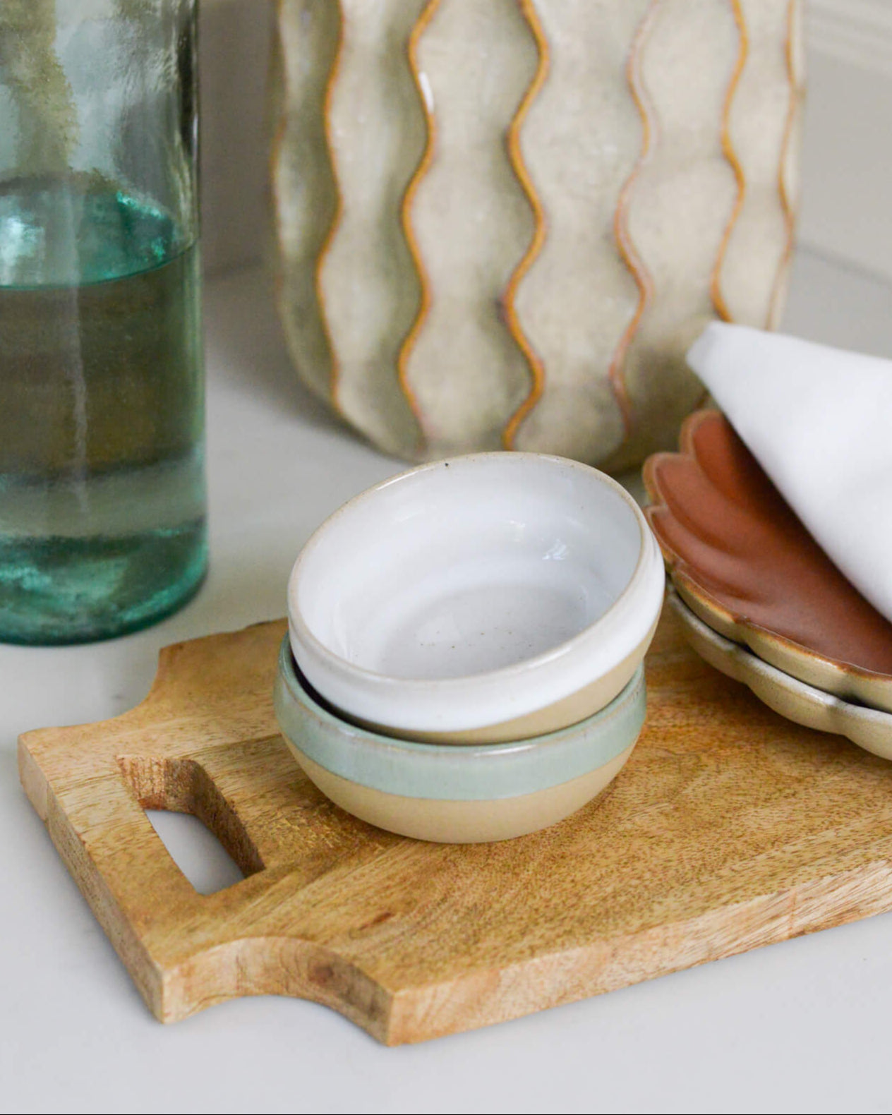 Decorative items including a glass bottle, ceramic bowls, and a wooden cutting board on a white surface.