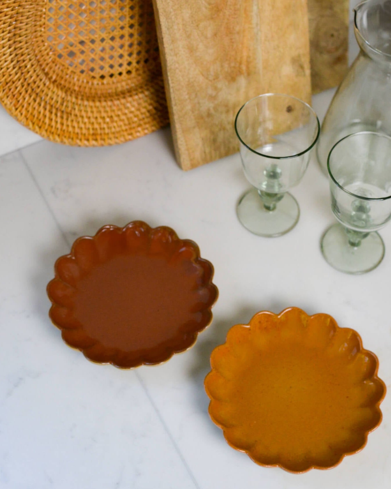 Two ceramic plates with scalloped edges on a white surface, with a rattan plate and wooden cutting board in the background.