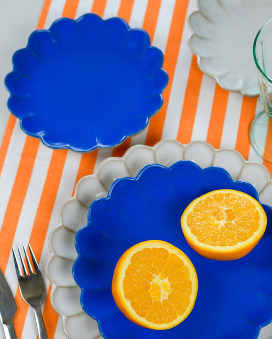 Blue scalloped-edge plates with sliced oranges on a striped orange tablecloth.