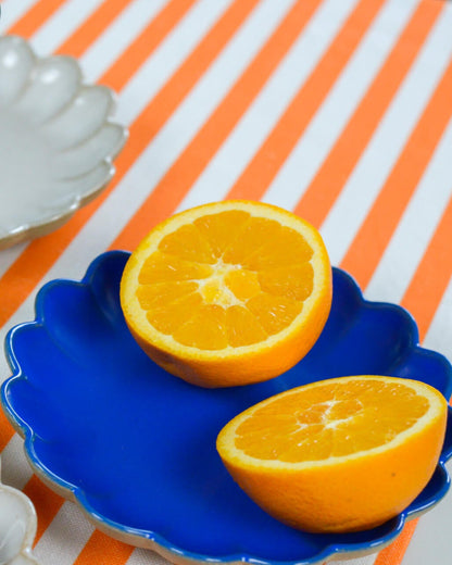 Sliced orange on a blue scalloped edge appetiser plate with an orange and white striped background