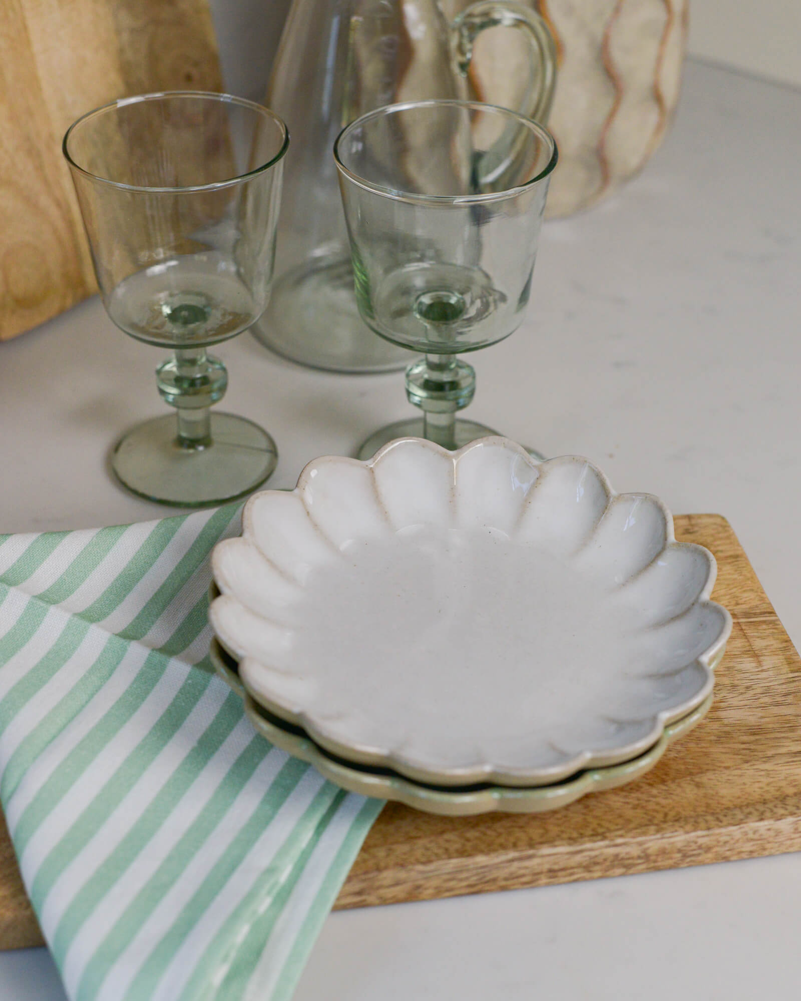 White scalloped edged dish on a wooden board with two glasses and a striped linen napkin in the background.