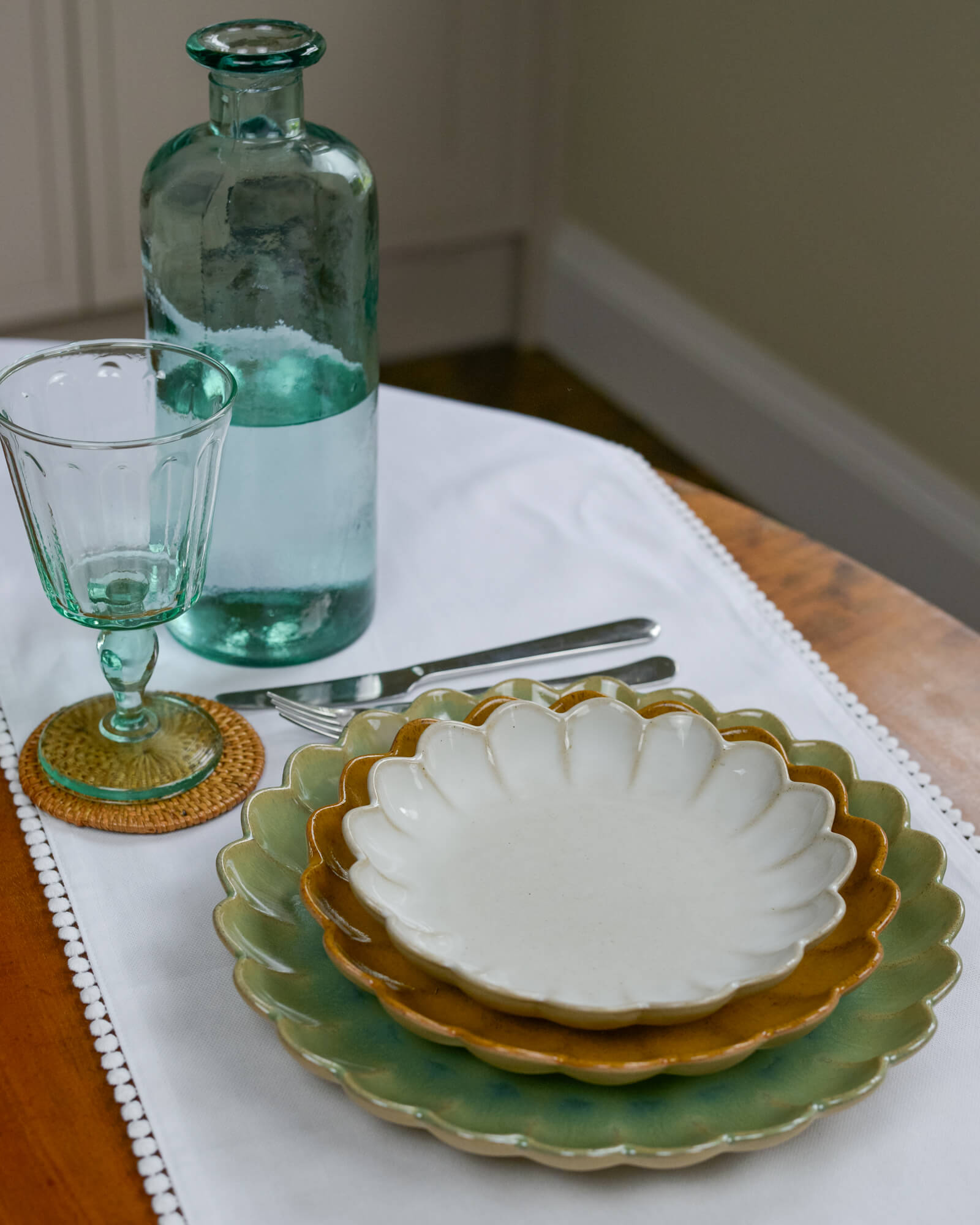 Set of layered ceramic scalloped edged plates with a glass bottle and glass on a table.