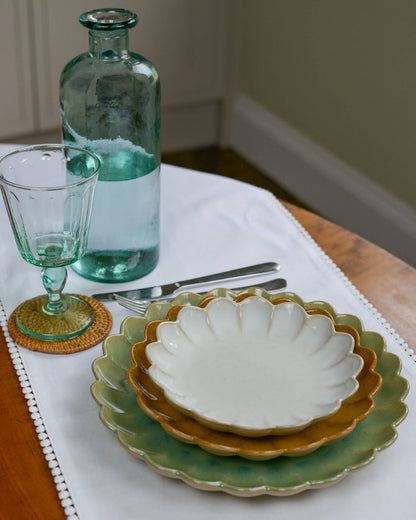 Set of layered ceramic scalloped edged plates with a glass bottle and glass on a table.