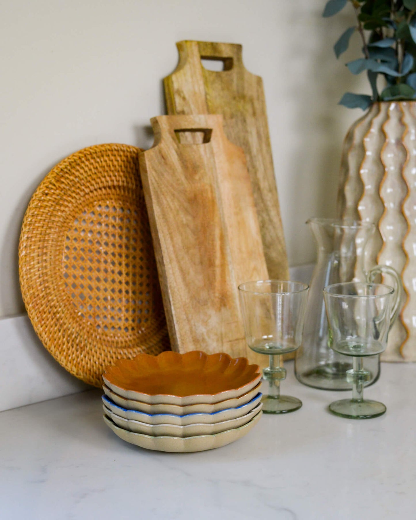 Wooden cutting board, rattan charger plate, ceramic bowl, and glassware on a white marble surface.