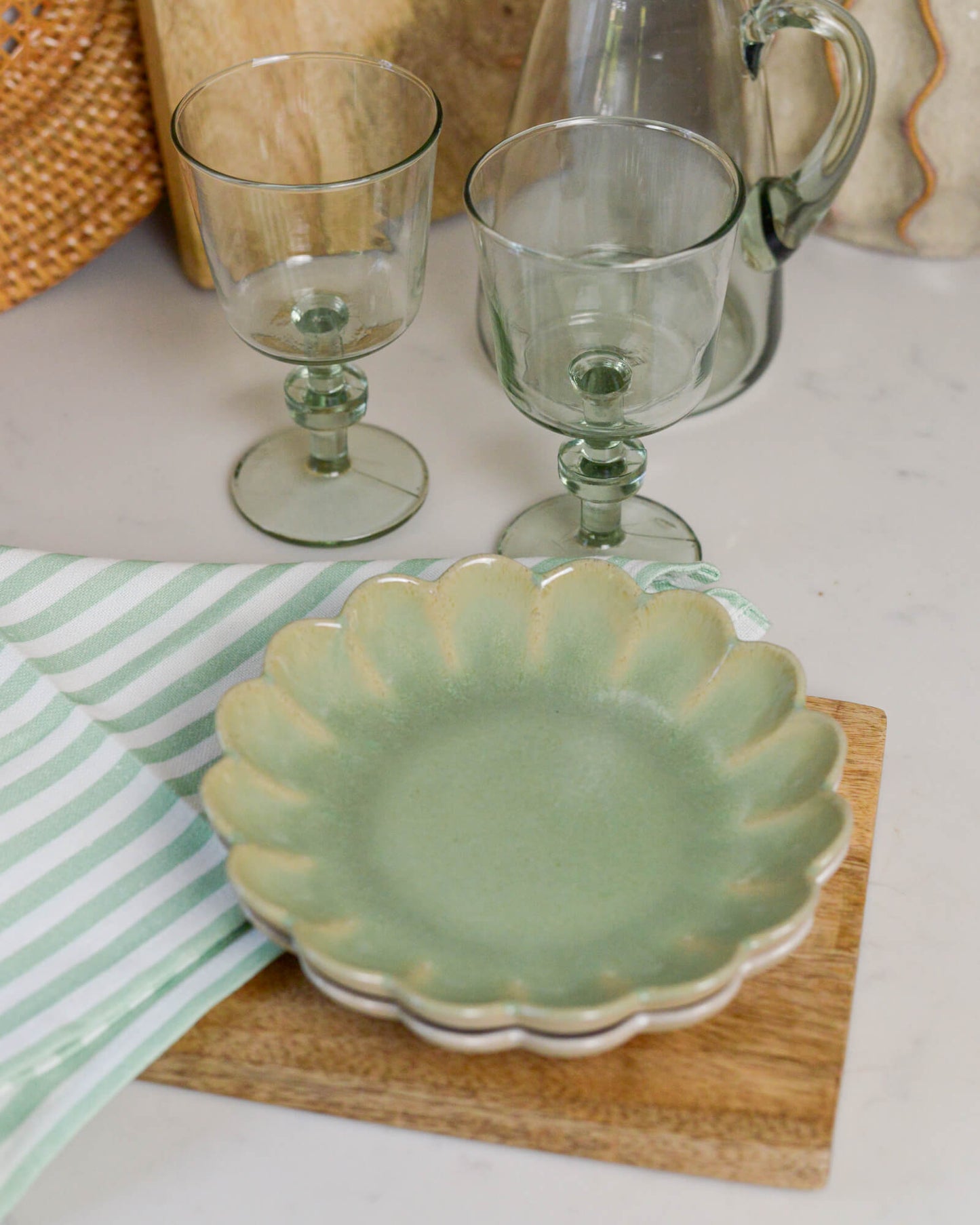 Green ceramic scalloped edged plate with two glass goblets on a white surface.