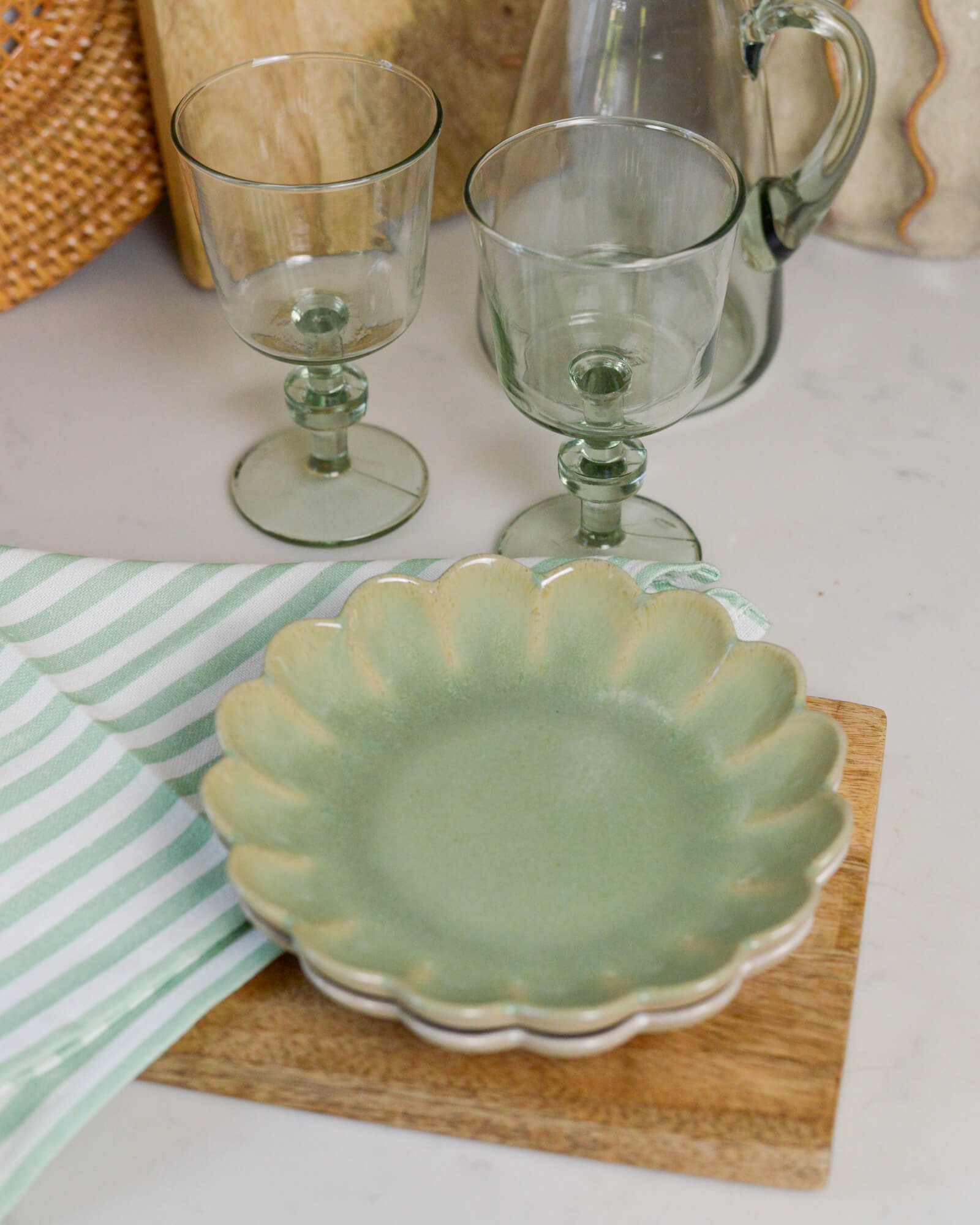 Green ceramic scalloped edged plate with two glass goblets on a white surface.