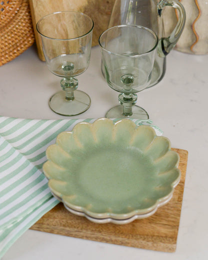 Green ceramic scalloped edged plate with two glass goblets on a white surface.