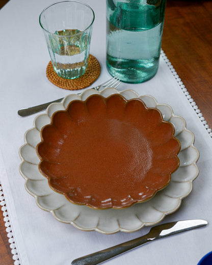 Ceramic plate with scalloped edge on a table setting with a glass and bottle.