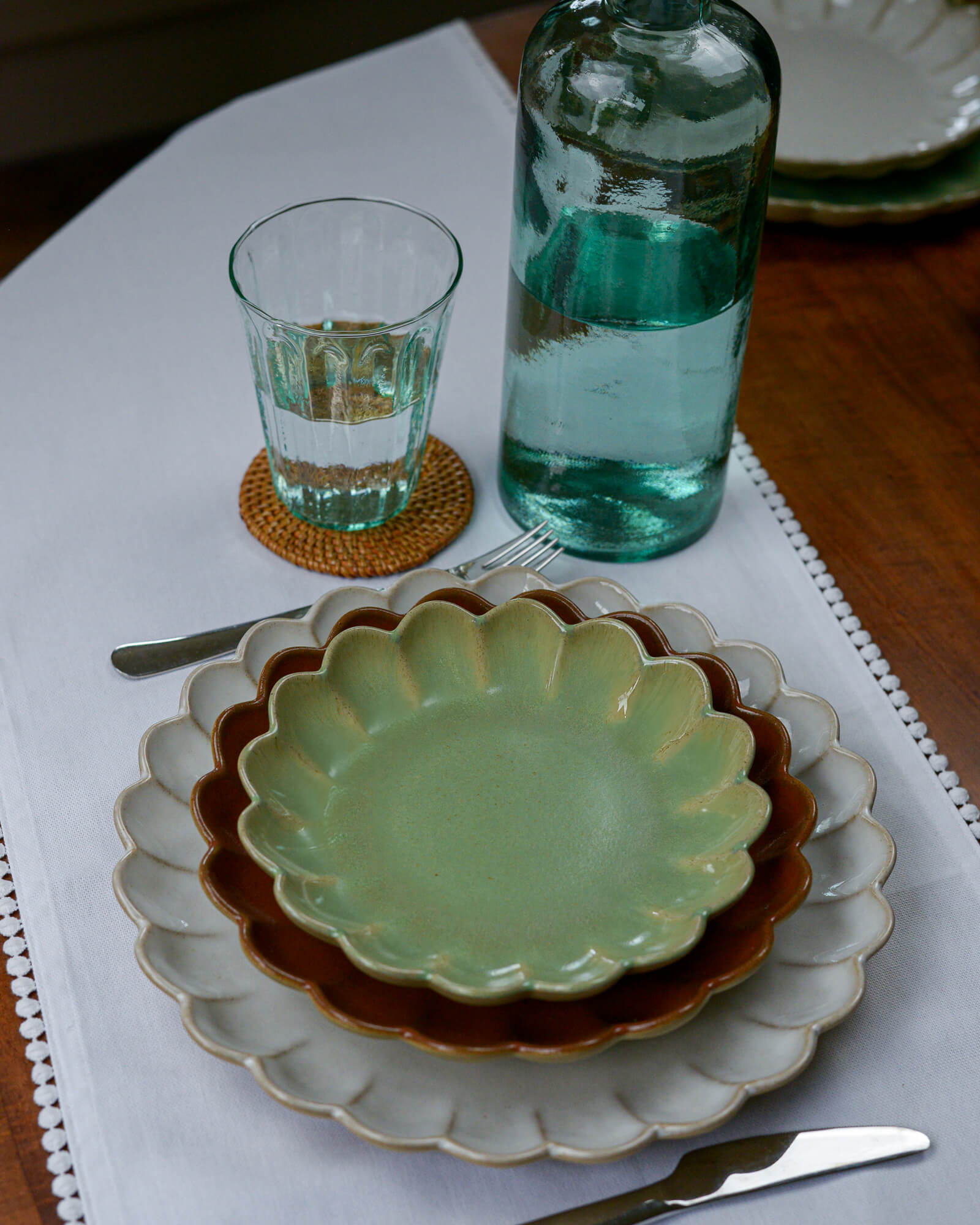 Set table with scalloped edge ceramic plates, glass, and bottle on a white tablecloth.