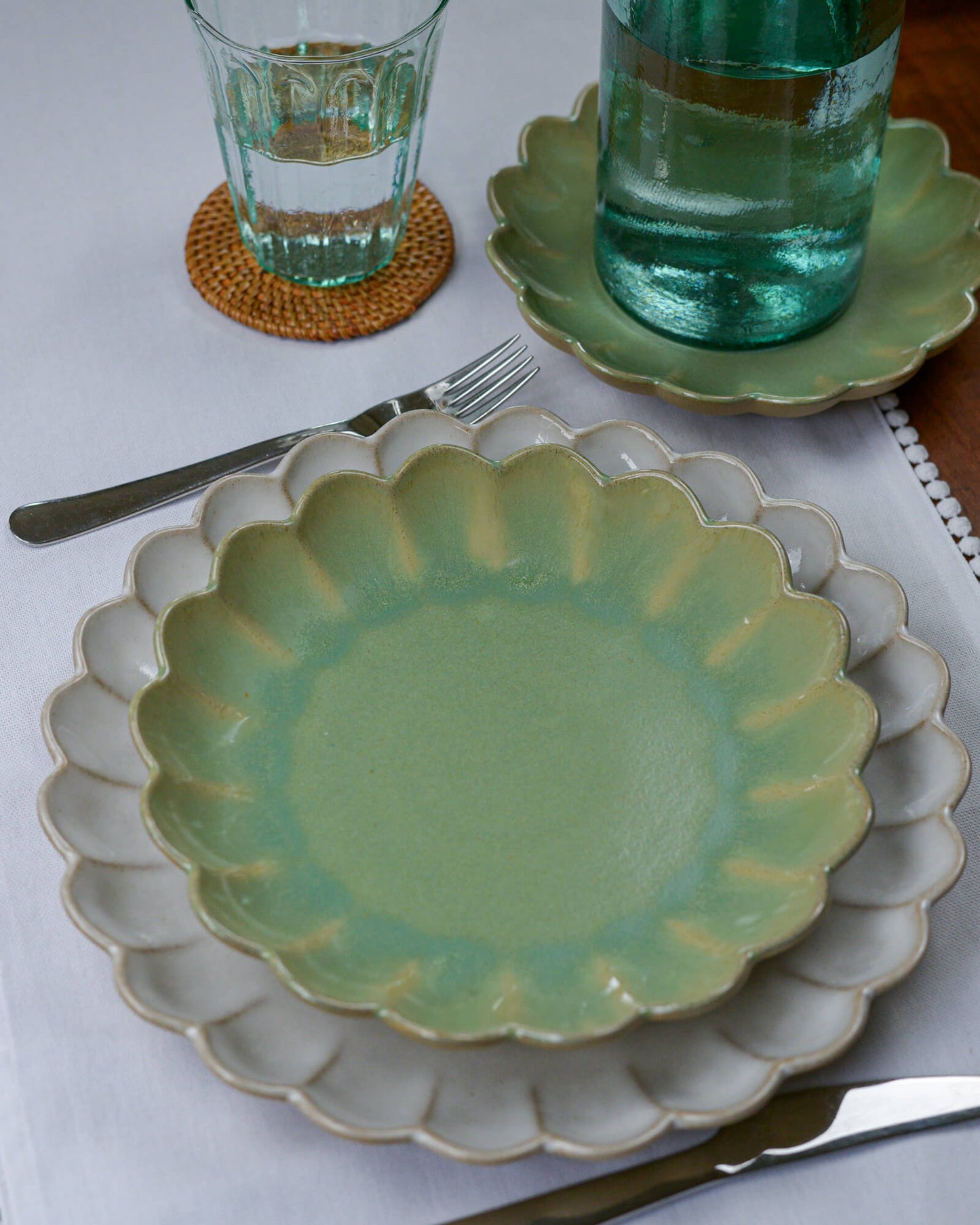 Green ceramic dessert plate with scalloped edge on a white tablecloth, with glasses and cutlery in the background.
