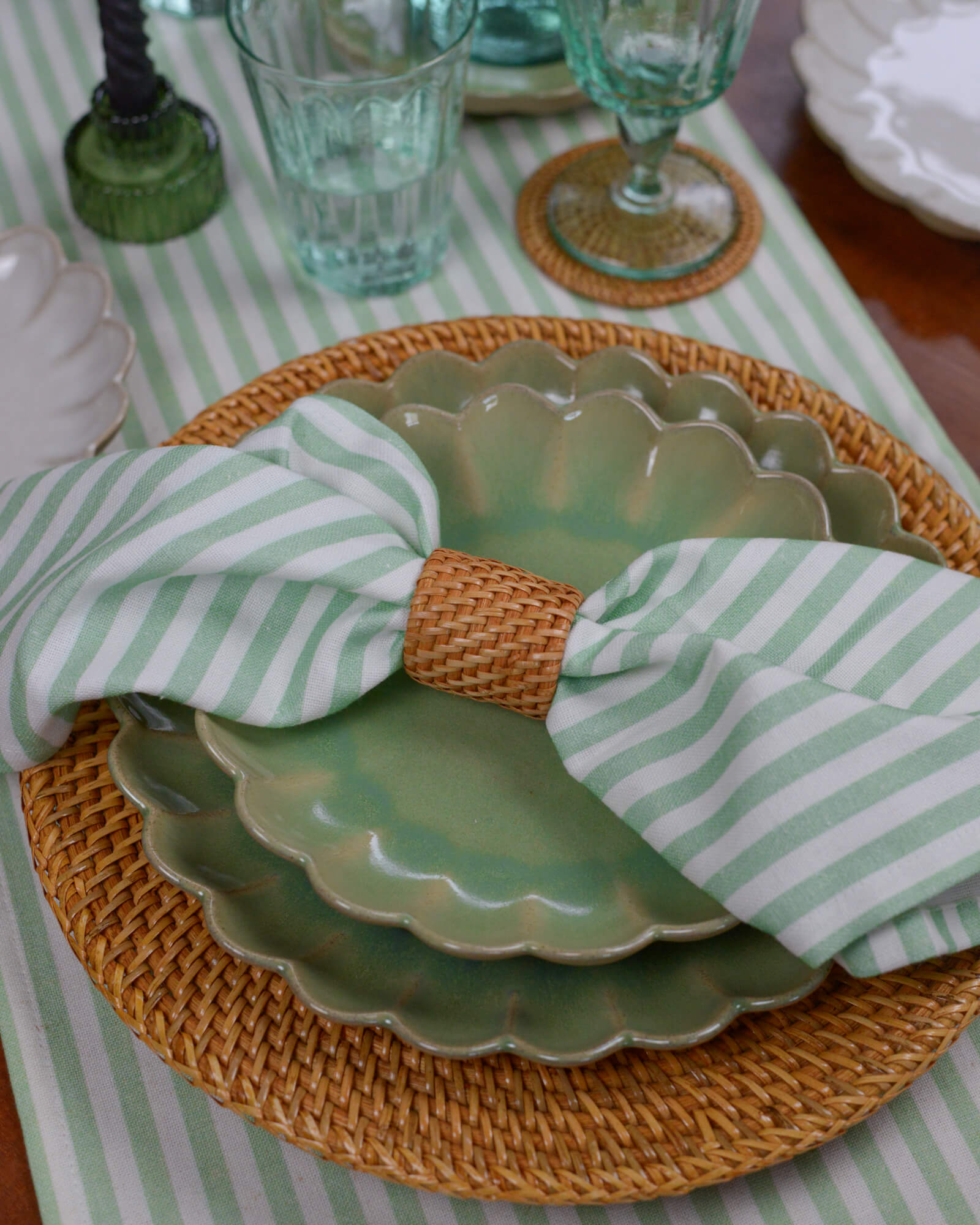Green scalloped edge plates with a striped napkin on a table with a green and white striped tablecloth.