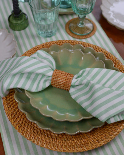 Green scalloped edge plates with a striped napkin on a table with a green and white striped tablecloth.