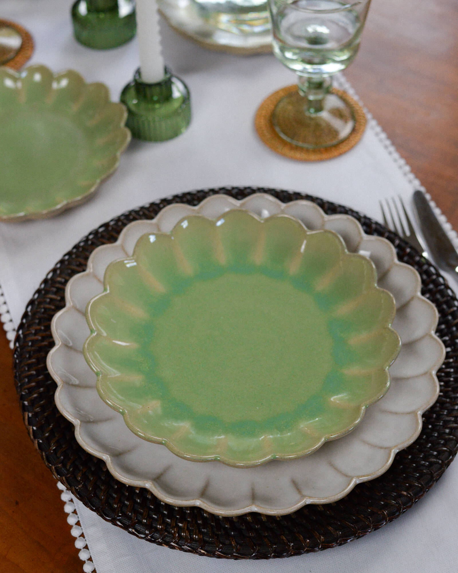 Green ceramic scalloped edge dessert plate on a white tablecloth with glasses and cutlery in the background