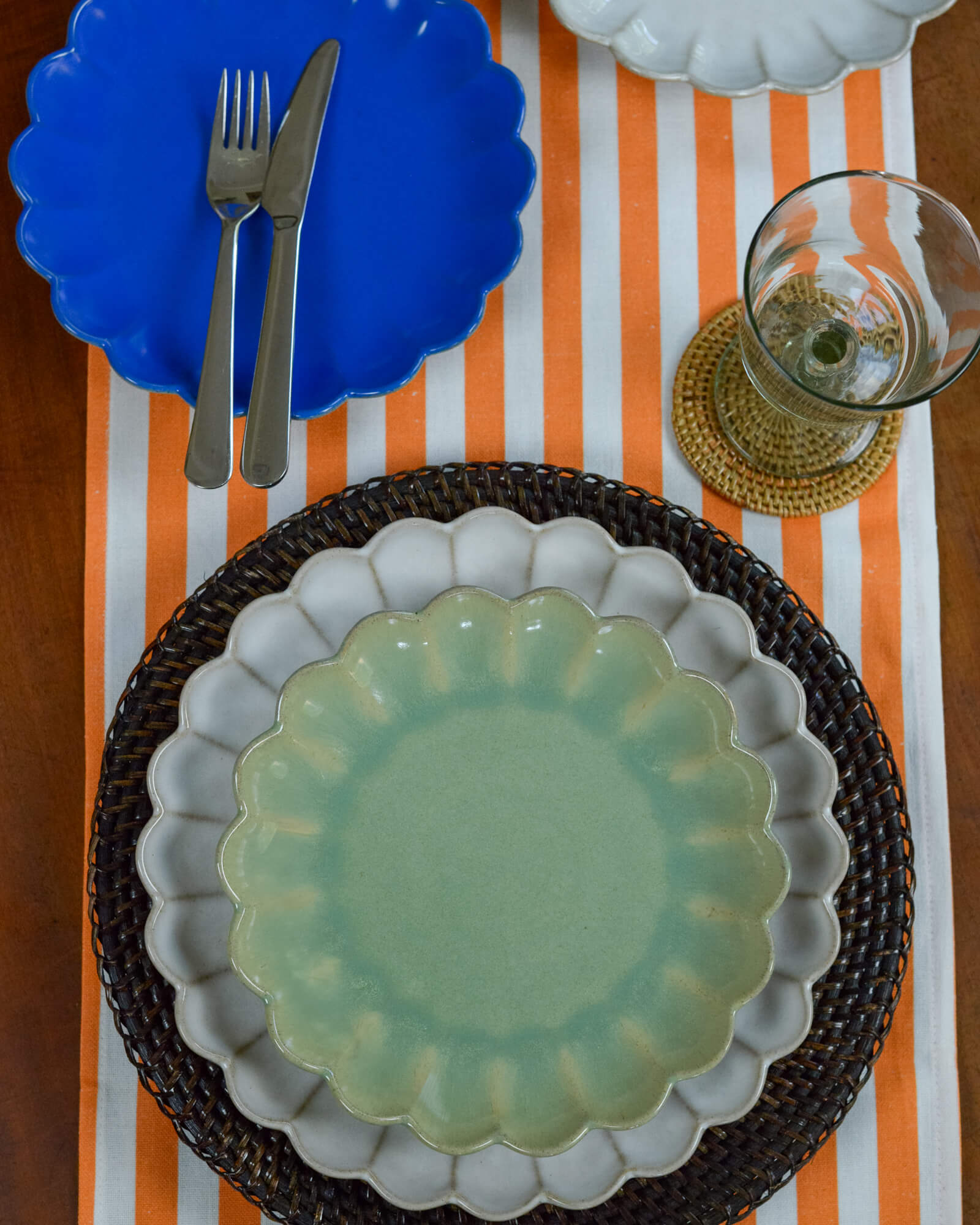 Table setting with a green scalloped edge plate, blue scalloped edge plate, and orange and white striped tablecloth.