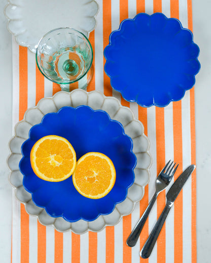 Blue and white scalloped edge plates with sliced oranges on a tablecloth with orange and white stripes.