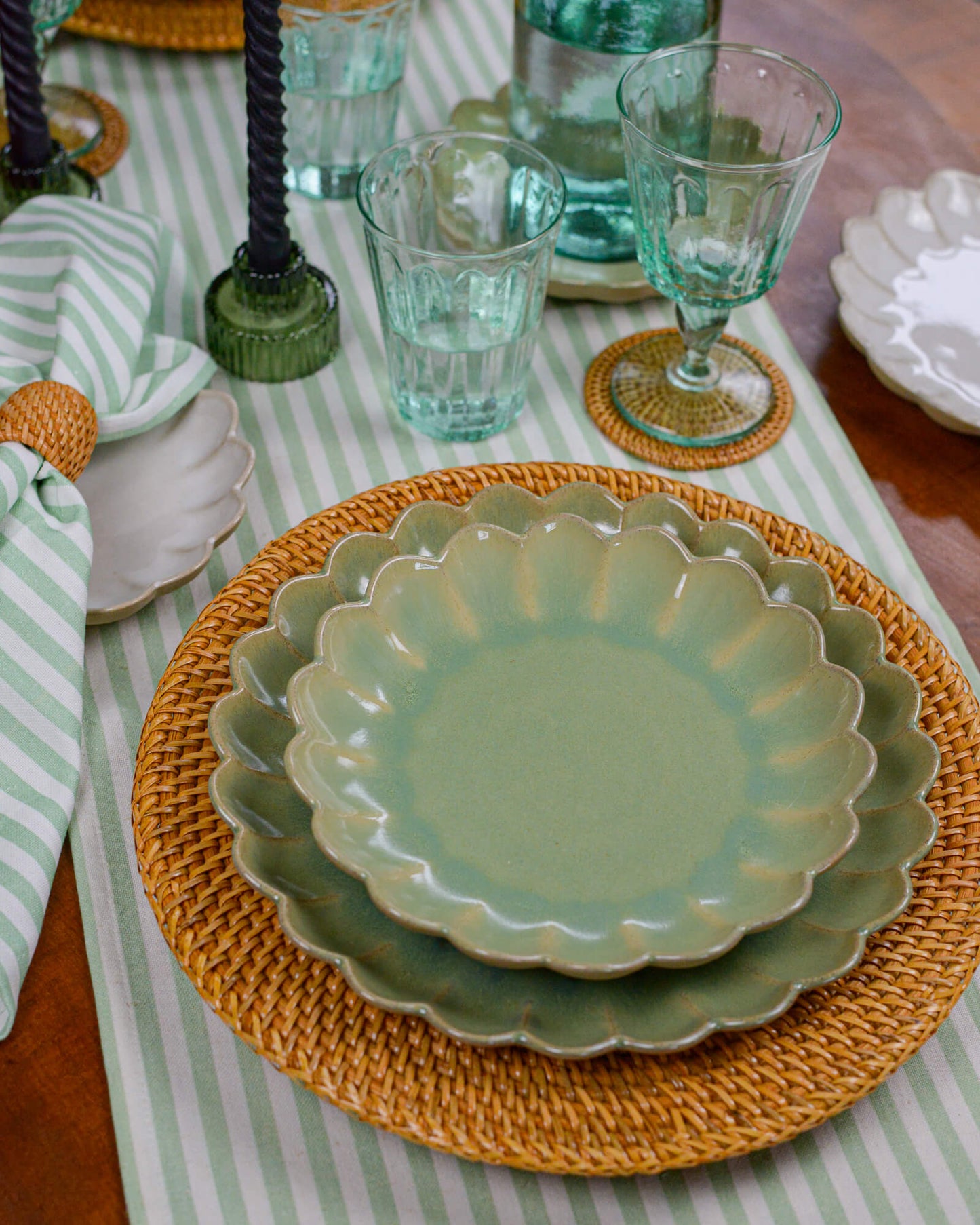 Green scalloped edged ceramic plate on a woven placemat with striped tablecloth and glasses in the background