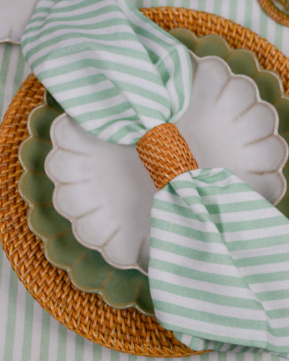Green and white striped napkin on a scalloped plate with a woven placemat.