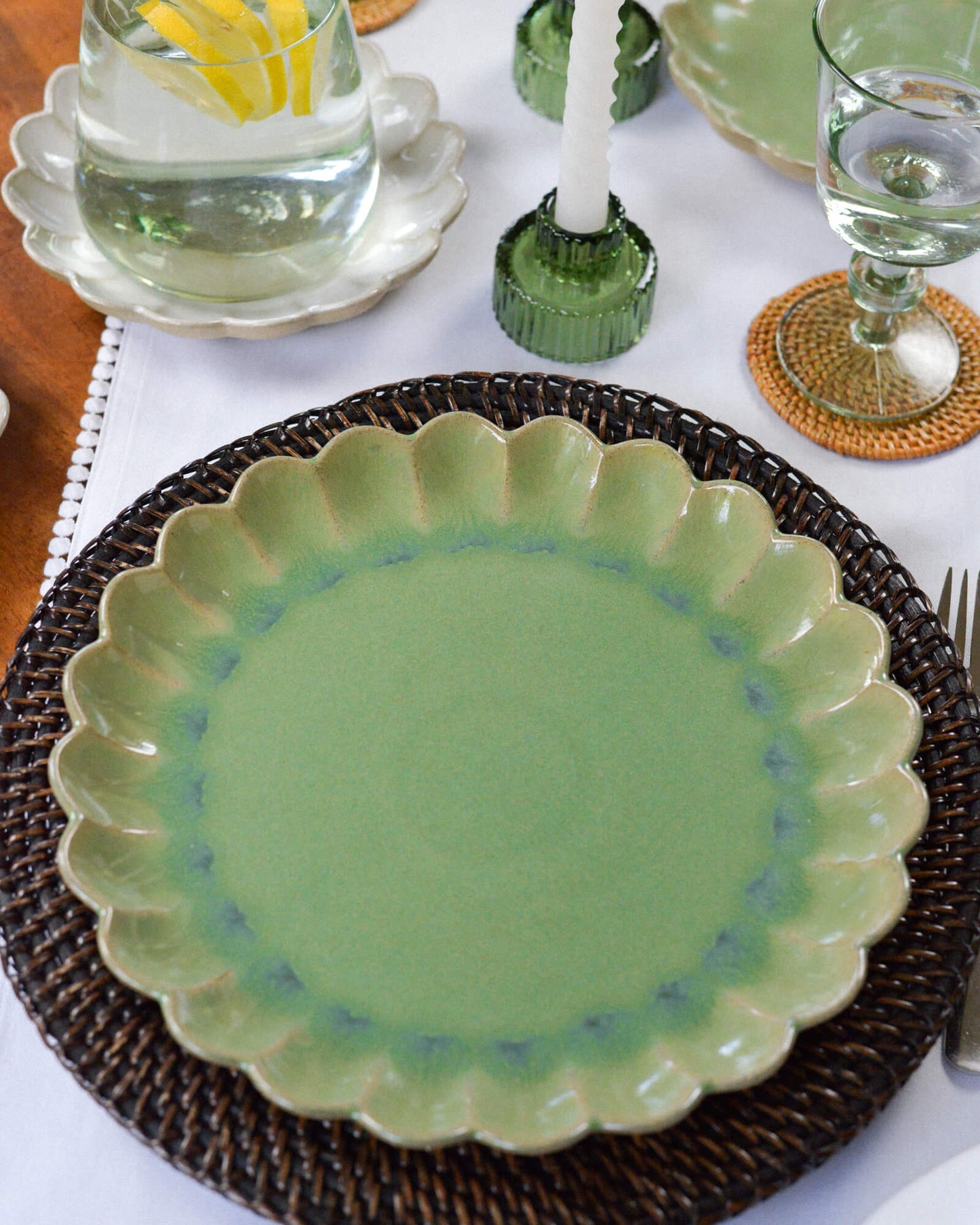 Green ceramic scalloped edged plate on a woven placemat with a table setting in the background