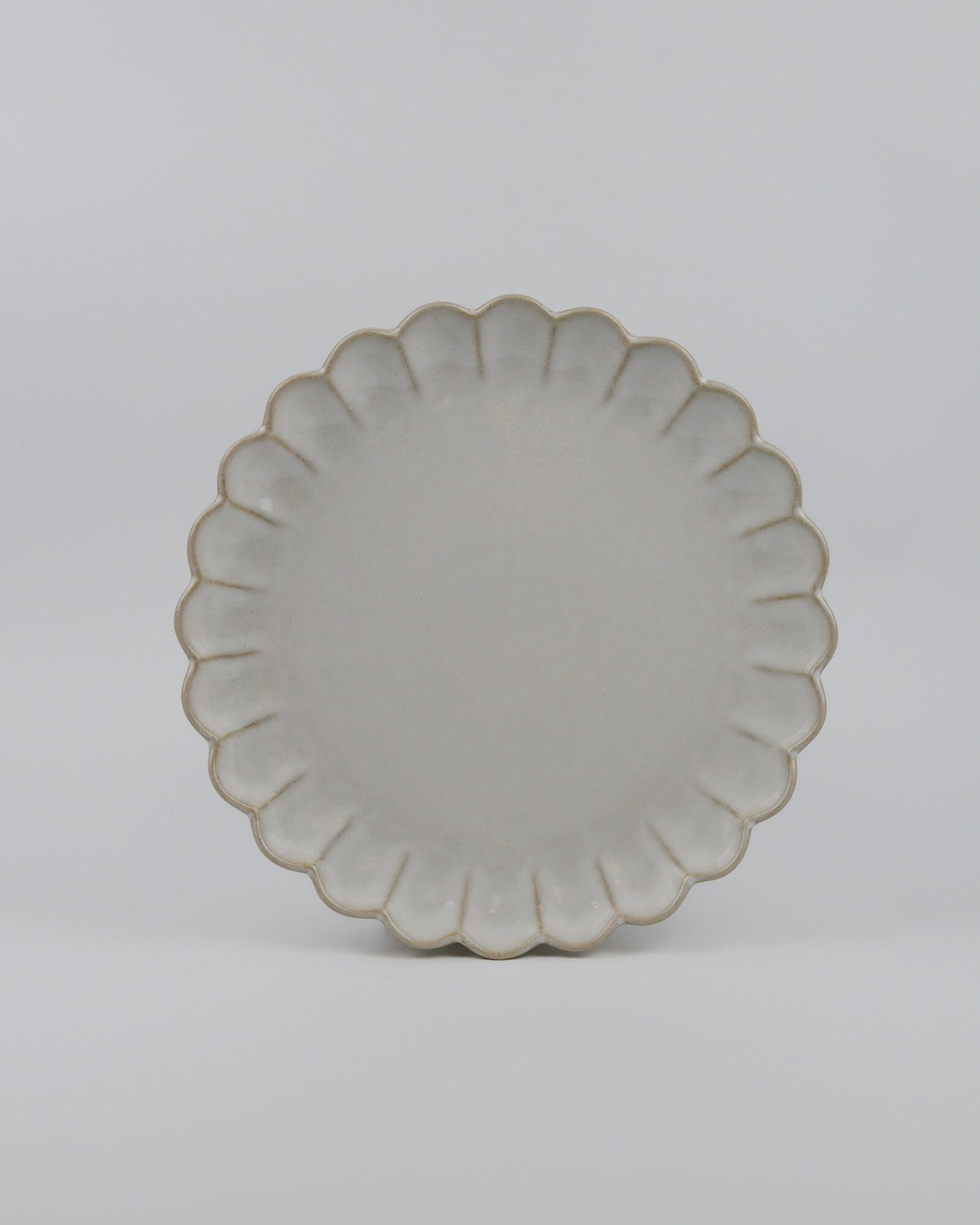 Round ceramic dinner plate with a decorative scalloped edge on a white background