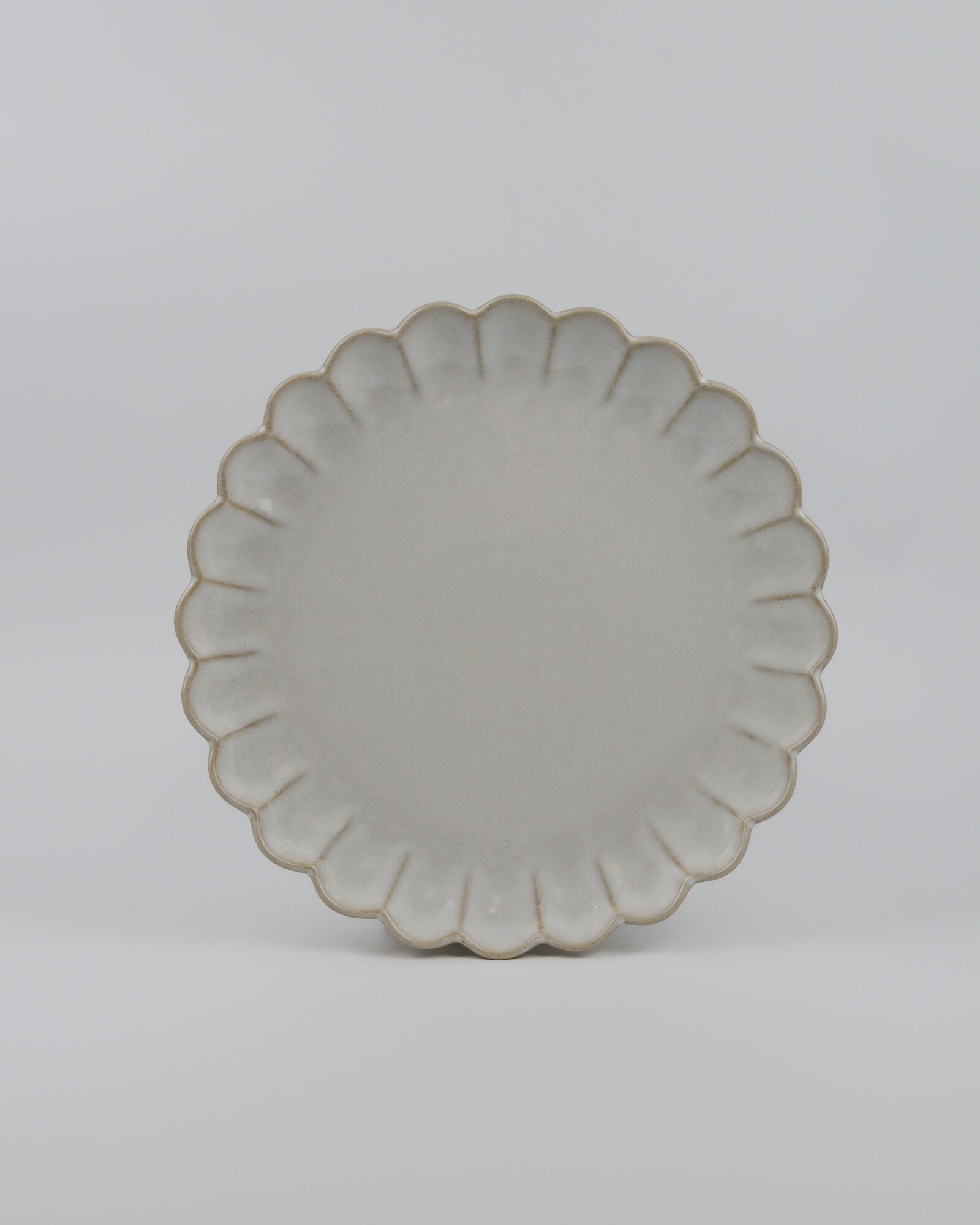 Round ceramic dinner plate with a decorative scalloped edge on a white background