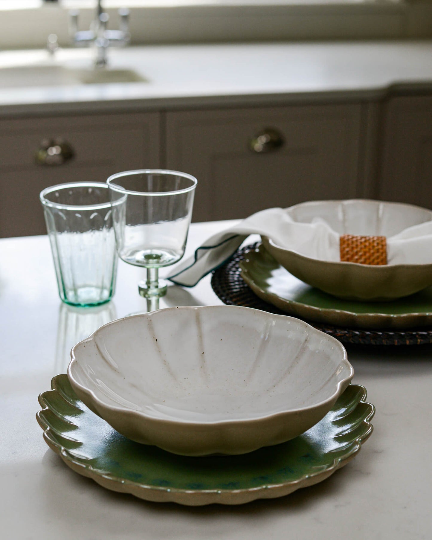 White stoneware Pasta bowl on a green scalloped edge stoneware plate and glasses on a kitchen counter