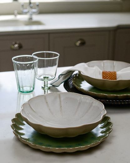 White stoneware Pasta bowl on a green scalloped edge stoneware plate and glasses on a kitchen counter