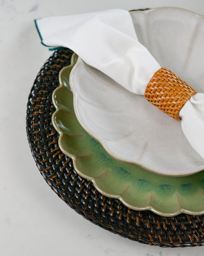 White scalloped pasta bowl, and woven napkin holder on a textured surface.
