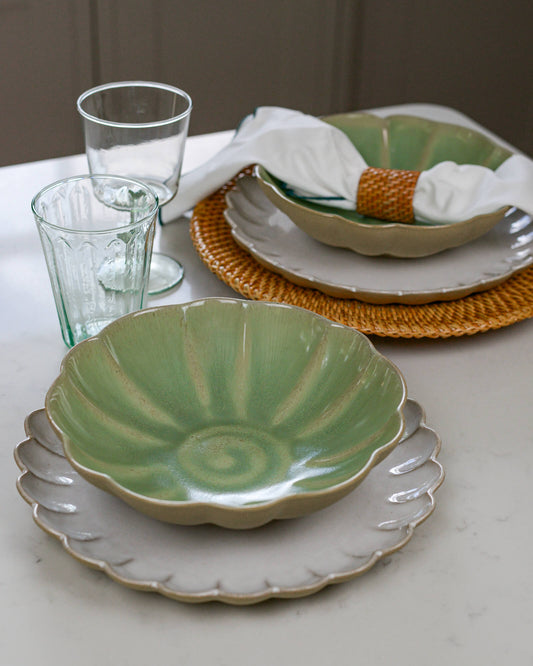 Dining table setting with green ceramic pasta bowl, white scalloped edge plates, and clear glasses on a neutral background.