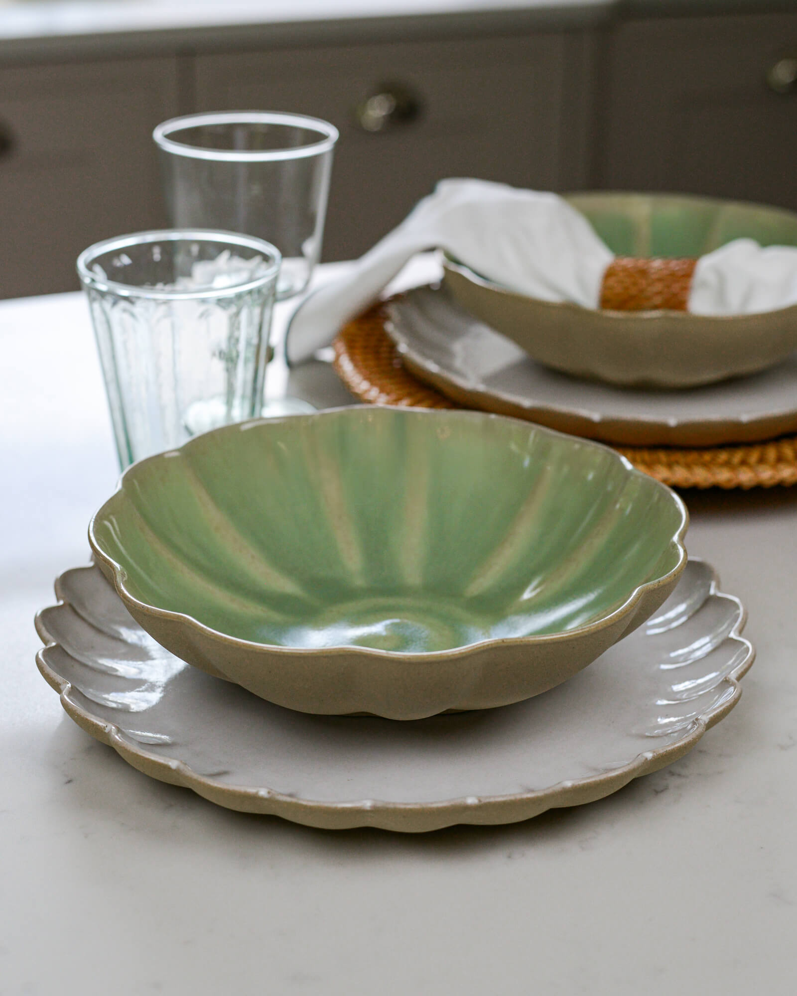 Green ceramic pasta bowl on a white scalloped edge plate on a marble surface 