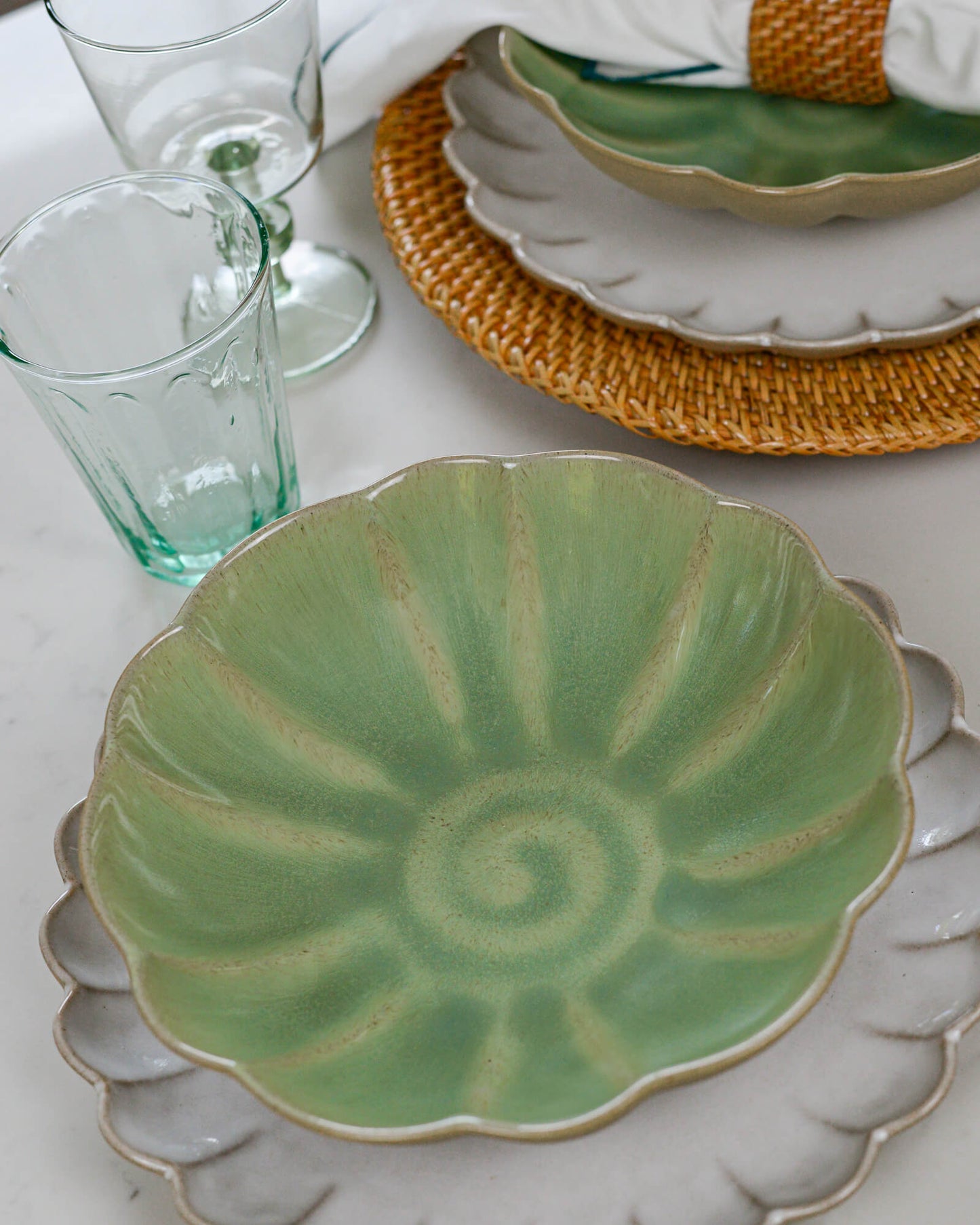 Green ceramic pasta plate with decorative pattern on a white marble surface with glasses and a woven placemat.