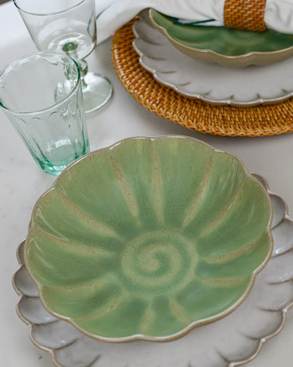 Green ceramic pasta plate with decorative pattern on a white marble surface with glasses and a woven placemat.