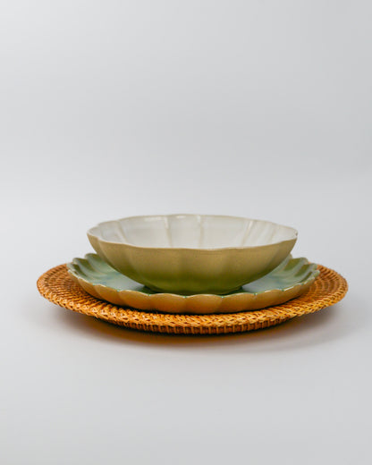 Set of ceramic stoneware scalloped plates and a pasta bowl with a woven placemat on a white background