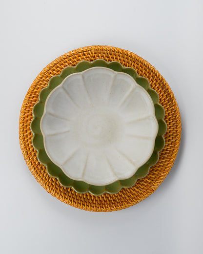 White ceramic pasta bowl layered on a green scalloped edge plate on a rattan charger plate against a white background