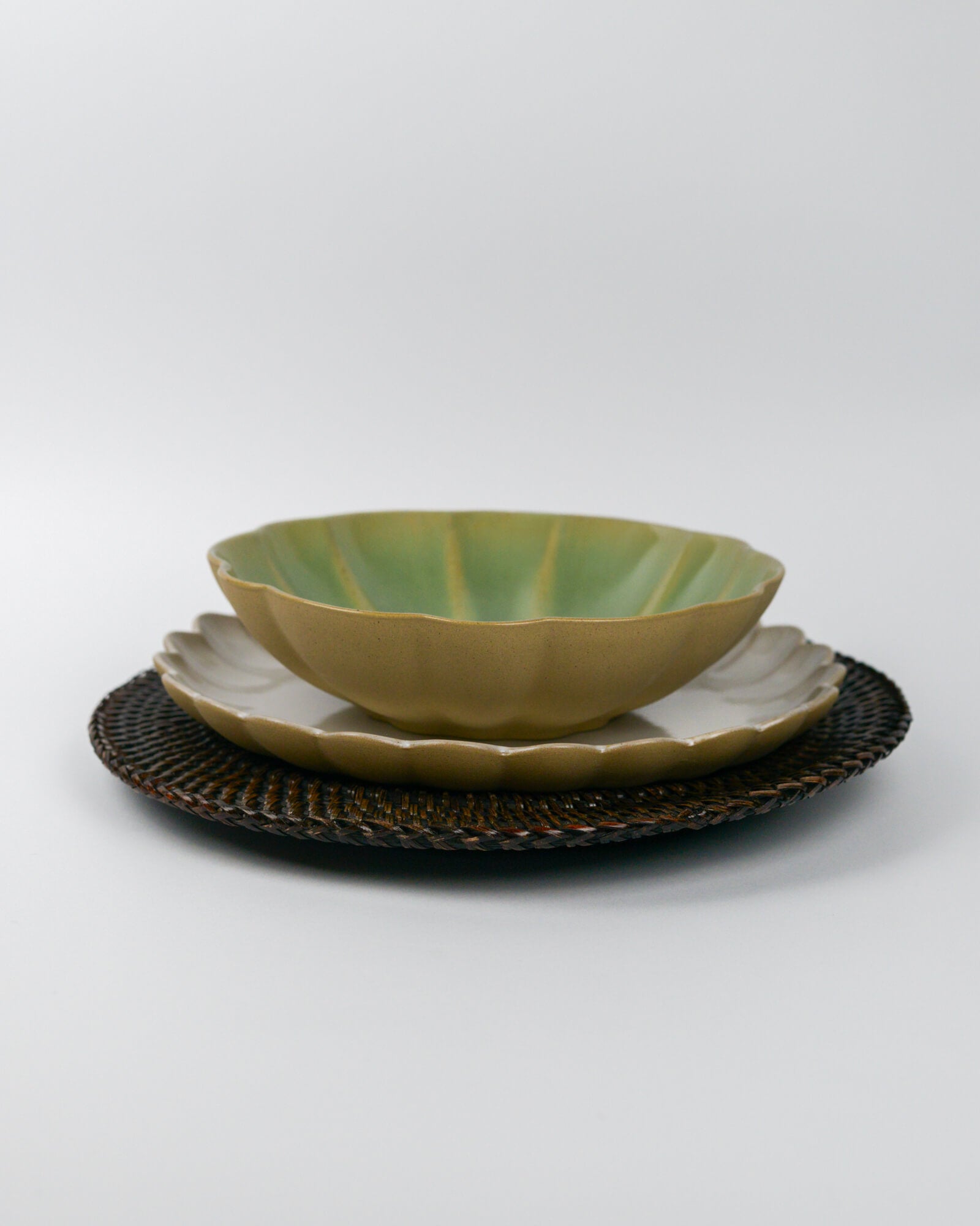 Green ceramic stoneware pasta bowl on a white scalloped edge plate on a rattan placemat with a white background