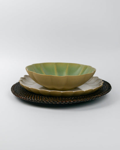 Green ceramic stoneware pasta bowl on a white scalloped edge plate on a rattan placemat with a white background