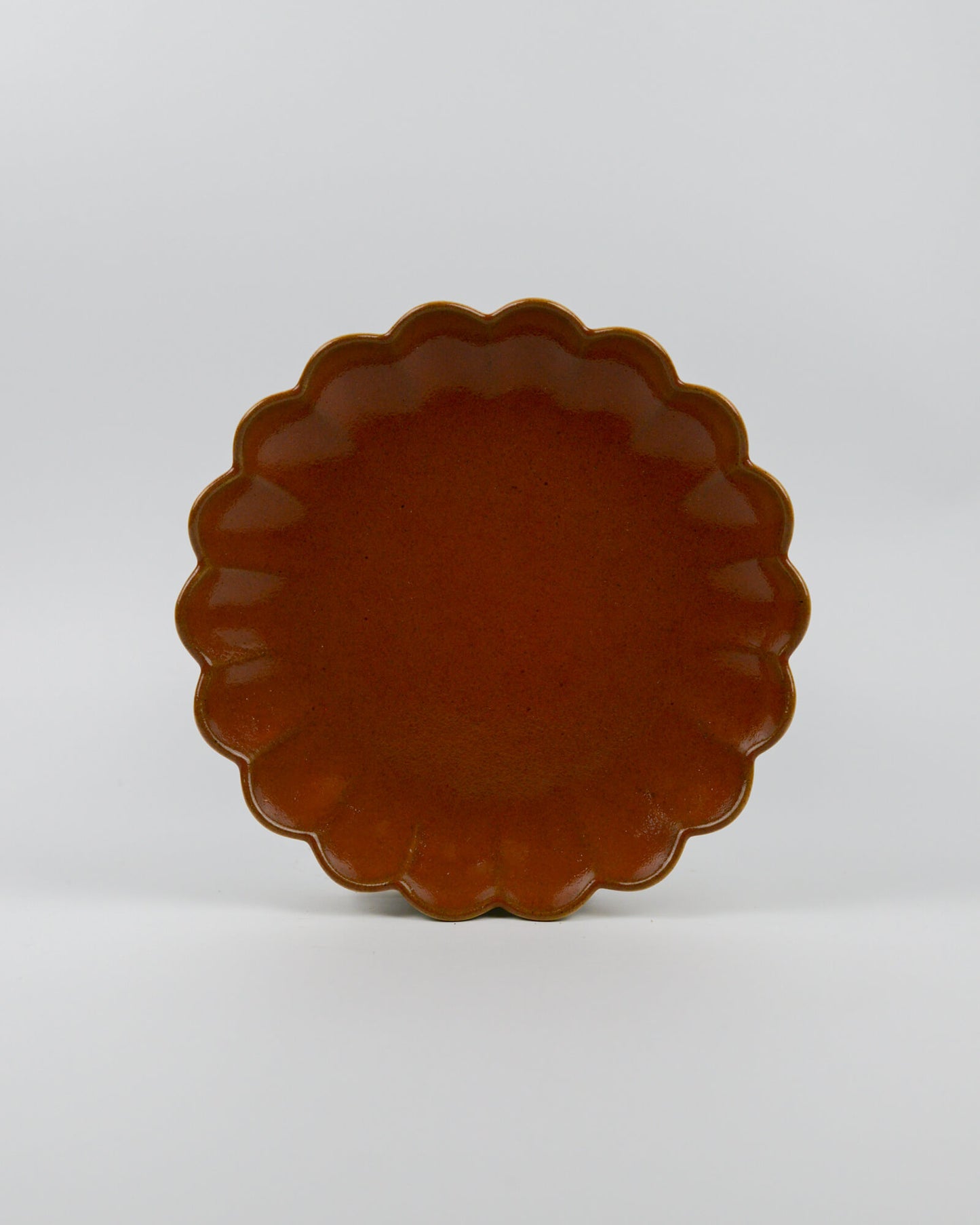 Rust coloured ceramic plate with scalloped edge on a white background