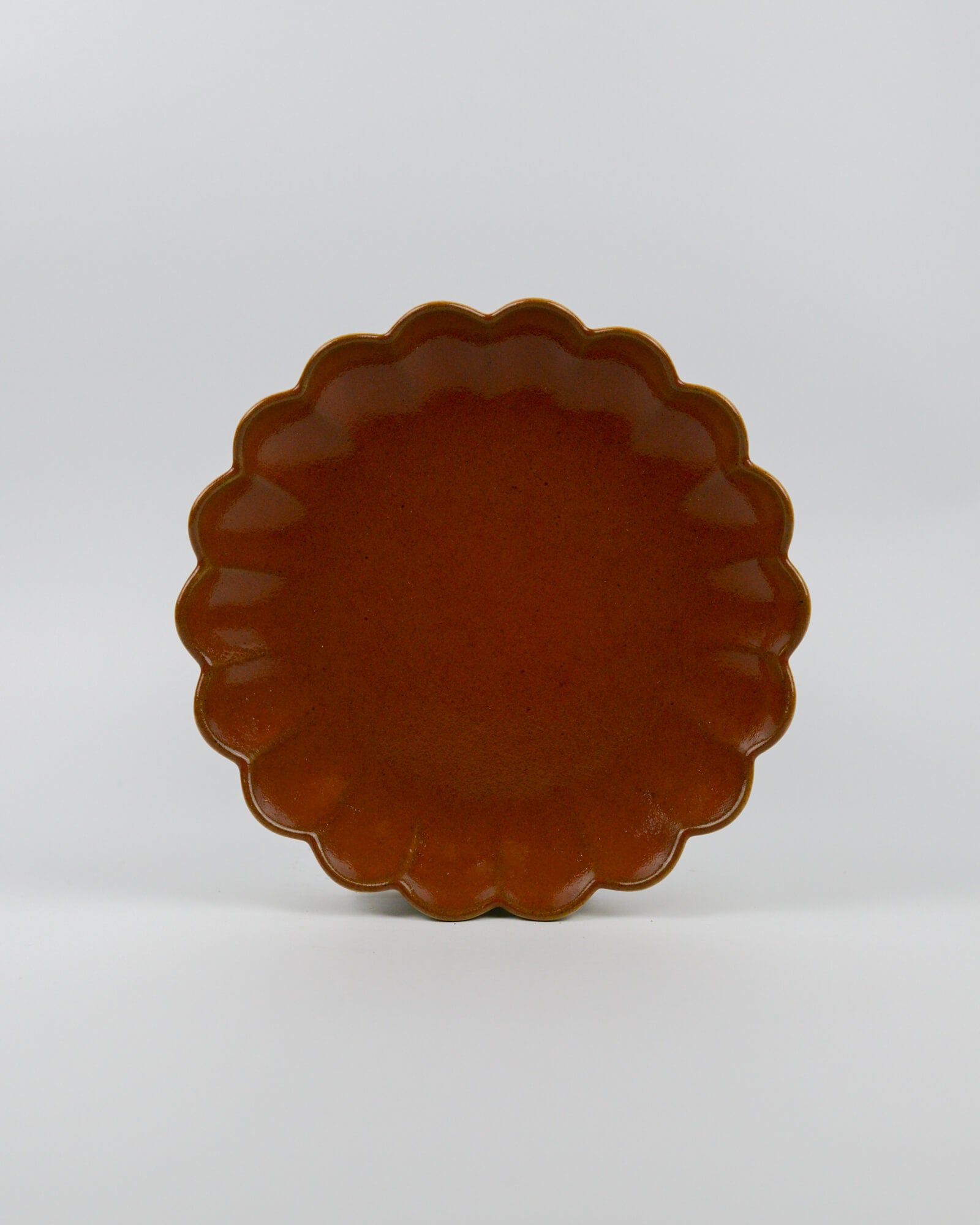 Rust coloured ceramic plate with scalloped edge on a white background