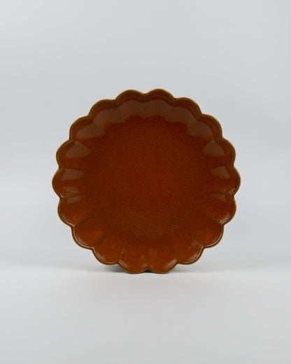 Rust coloured ceramic plate with scalloped edge on a white background