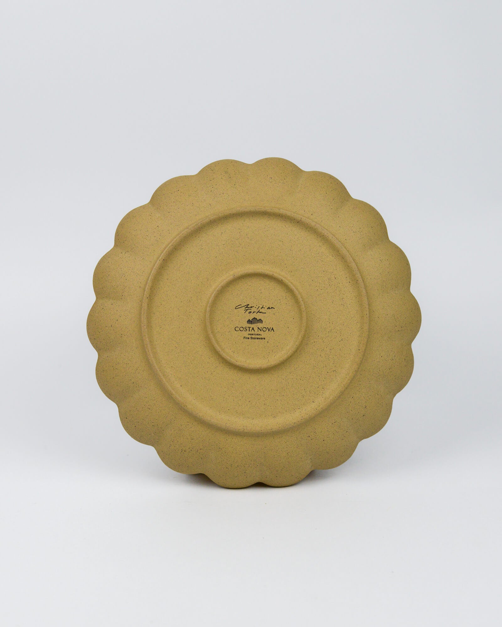 Underside of a stoneware ceramic plate with scalloped edge on a white background