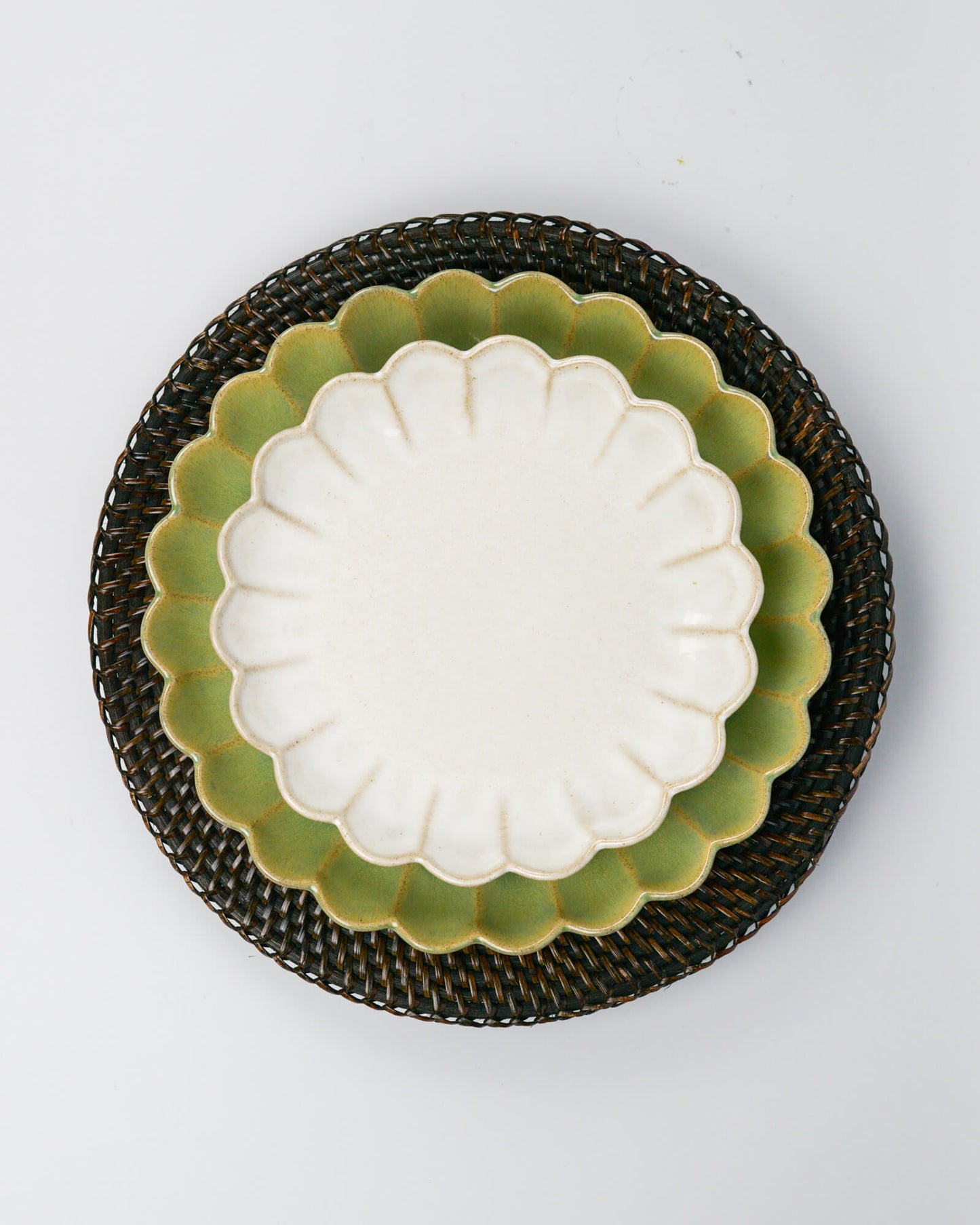 White scalloped dessert plate with green scalloped dinner plate underneath on a rattan placemat against a white background