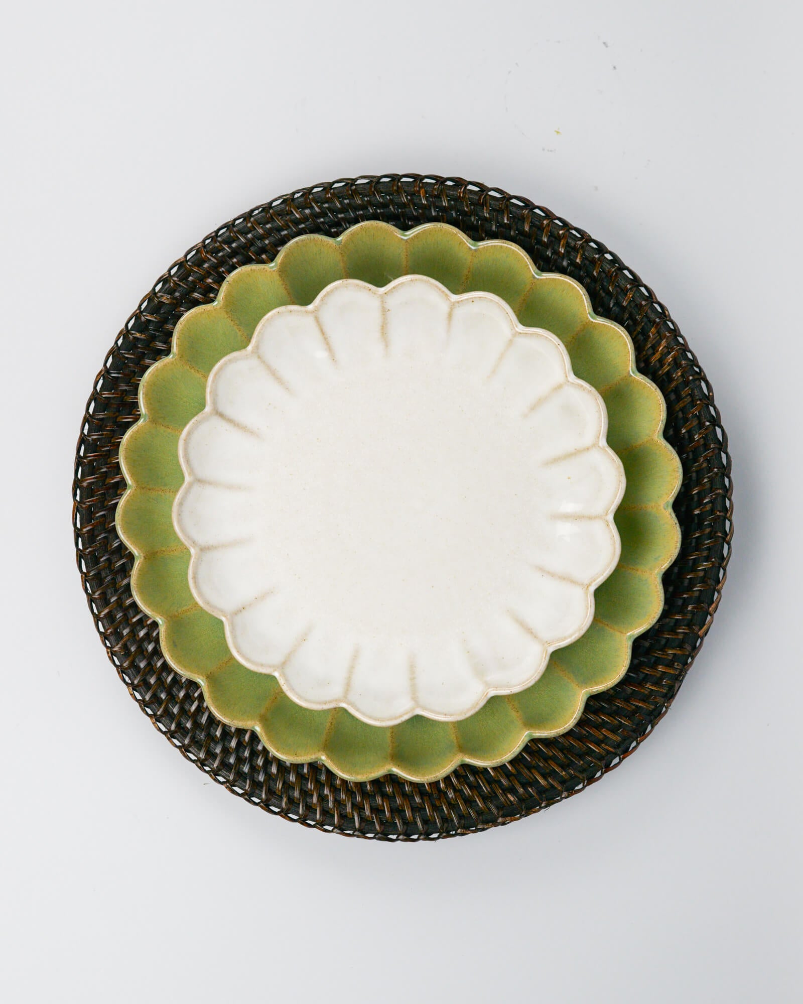 White scalloped dessert plate with green scalloped dinner plate underneath on a rattan placemat against a white background